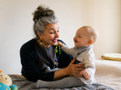 Frau mit Dutt sitzt lächelnd neben fröhlichem Baby.
